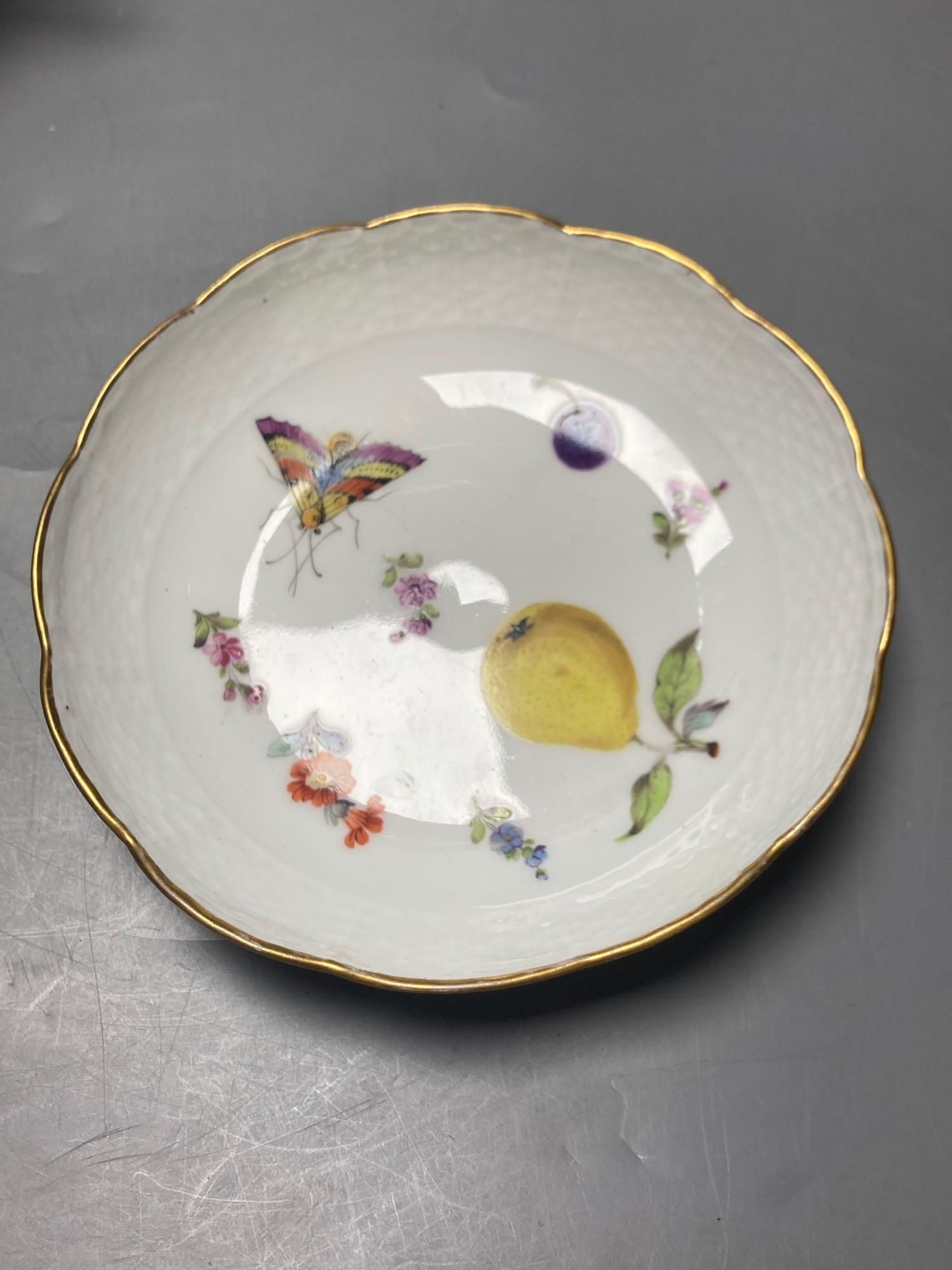 A Meissen cup and saucer, factory seconds, decorated with fruit and butterflies and lined with gilt